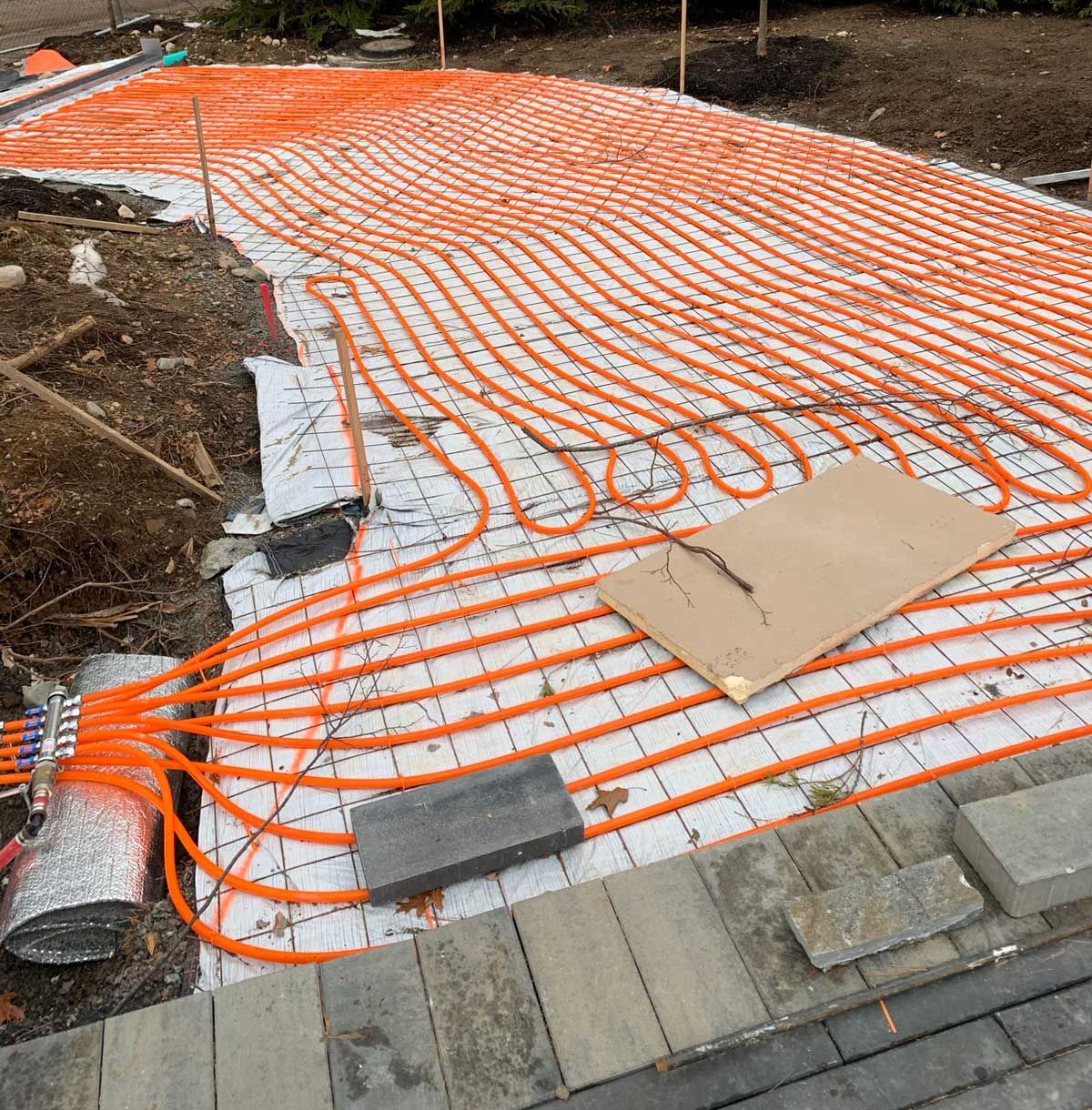 Orange radiant heating tubes laid out on a concrete base.