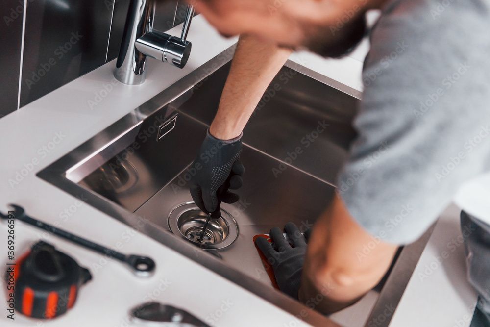 Person unclogging a stainless steel sink with a gloved hand in a kitchen sink area