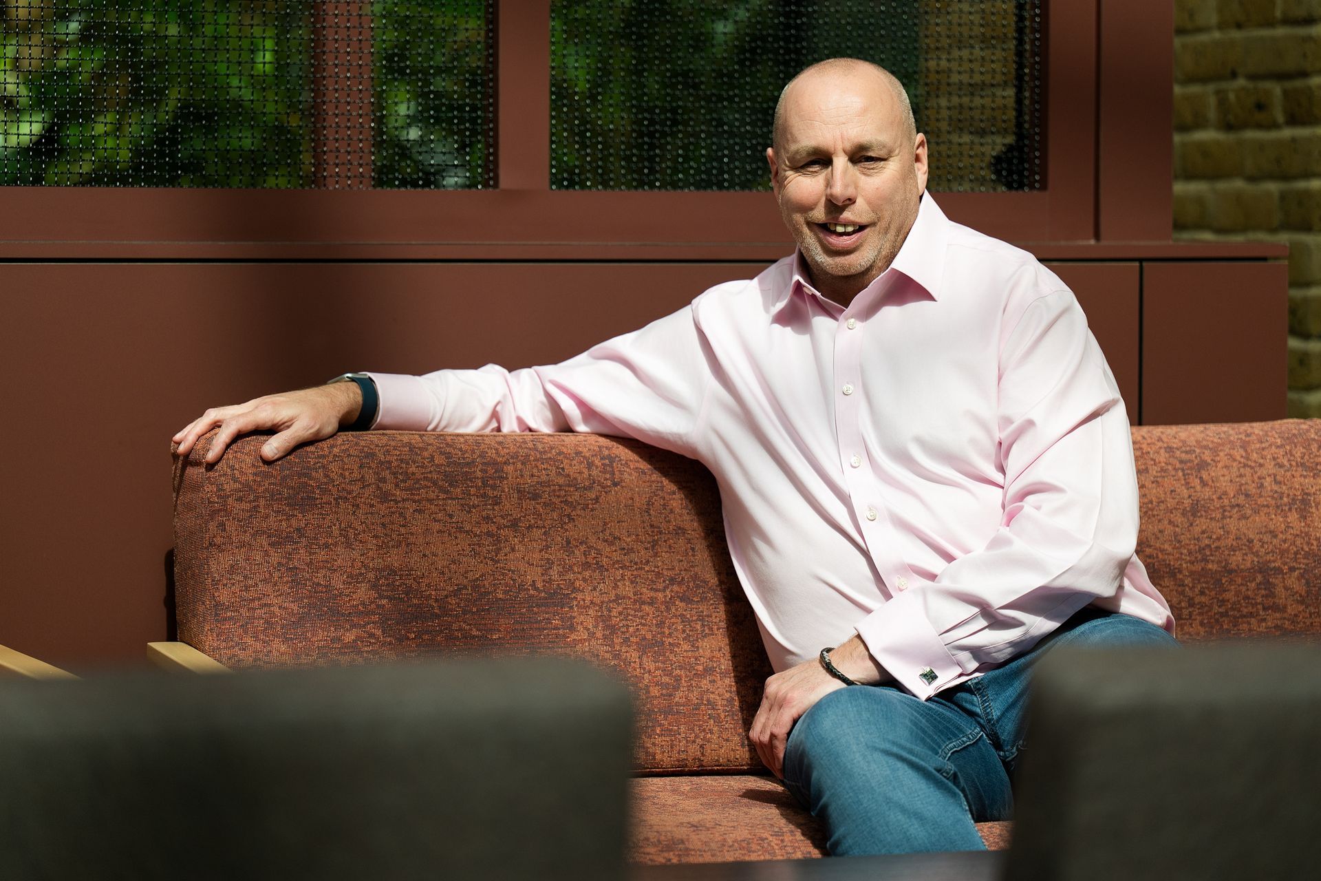 Man in a light pink shirt sitting on a couch outdoors in sunlight