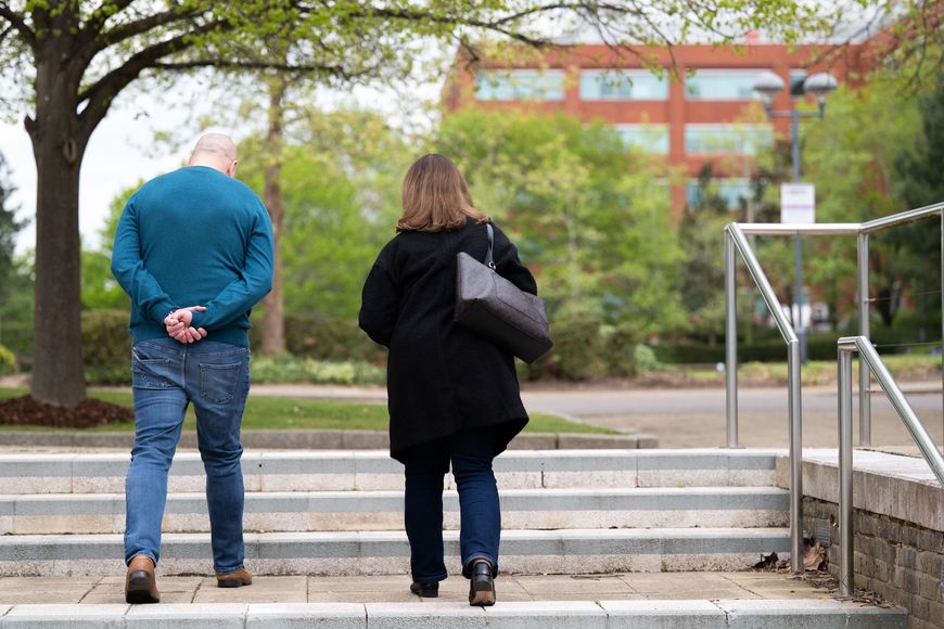 Two people standing at the bottom of outdoor steps near a building, one with a black bag.