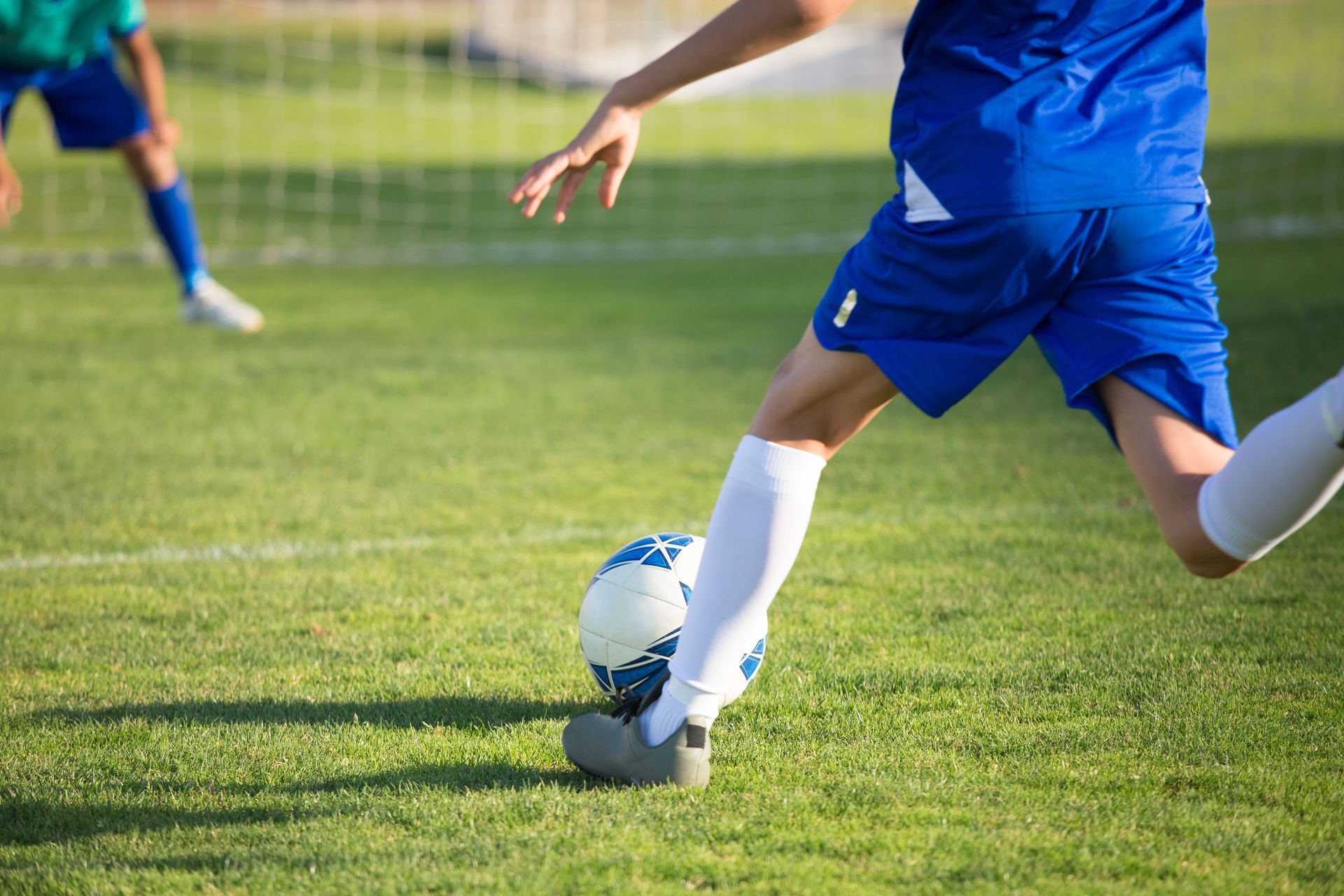 Soccer player in blue uniform kicking a ball on a grassy field