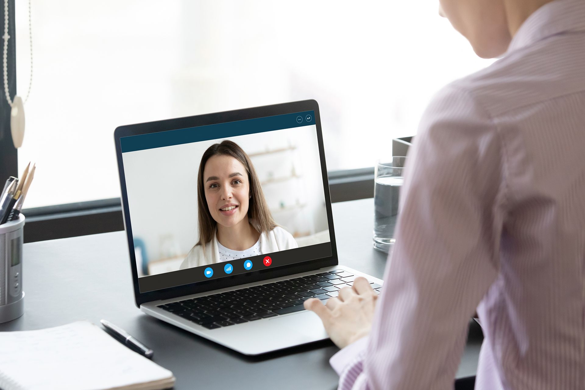Una mujer está sentada en un escritorio usando una computadora portátil para tener una videollamada con otra mujer.