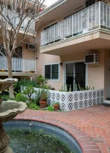 A courtyard with a tiered fountain, red brick walkway, lush greenery, and balconies of a modern apartment building.