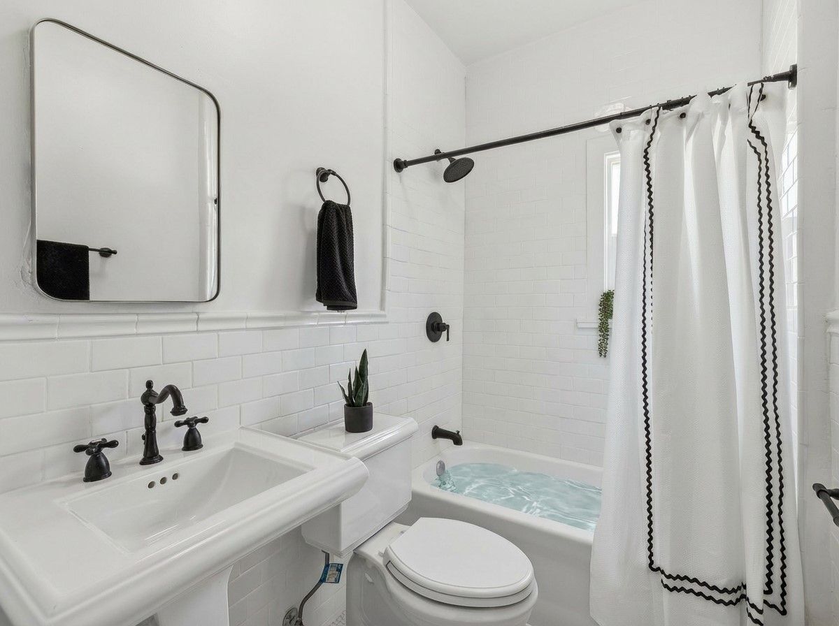A bright, modern bathroom with white subway tiles, a pedestal sink, black fixtures, and a bathtub with shower curtain.