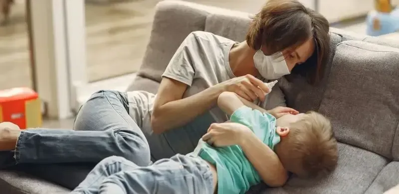 close up photo of a mother wearing face mask, embracing her baby, and feeding with small bottle