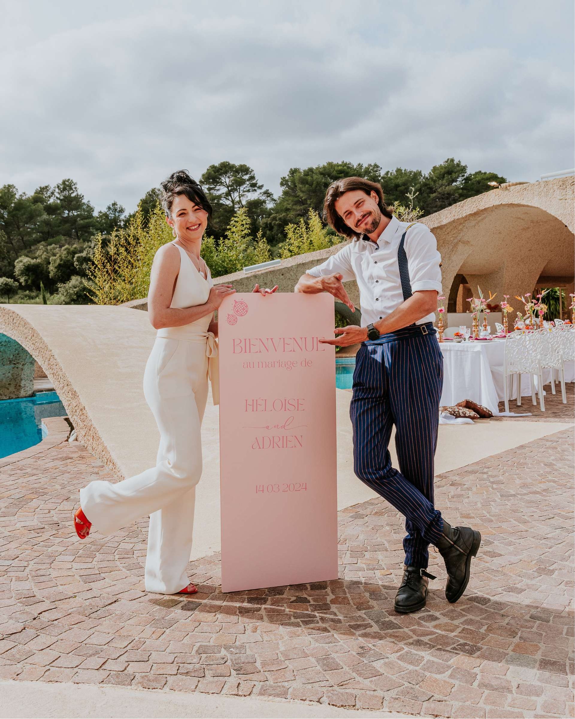 Une mariée et un marié se tiennent à côté d'un panneau rose.