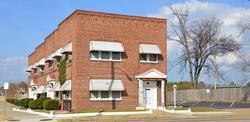 Brick apartment building with white awnings and a small entrance porch on a street corner