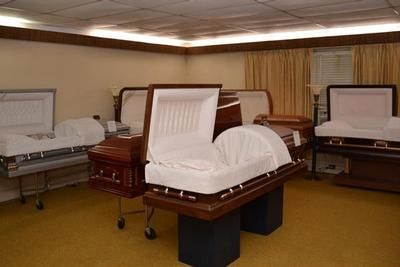 Three open caskets in a funeral home viewing room with beige walls and wood trim