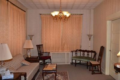 Cozy living room with beige sofa, wooden chairs, lamps, and peach curtains around a window