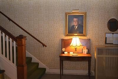 Staircase landing with a lit lamp on a small table beneath a framed portrait.