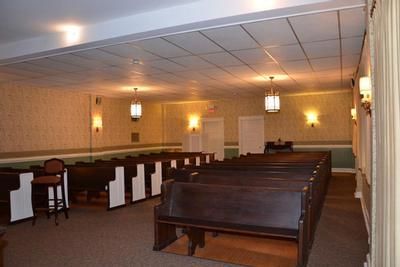 Empty church interior with wooden pews, warm wall sconces, and white ceiling tiles