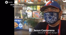 A man wearing a mask and a hat is sitting in a restaurant.