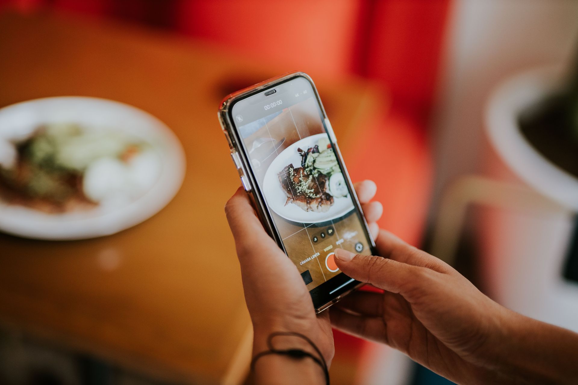 Hands photographing a plated meal with a smartphone at a restaurant table