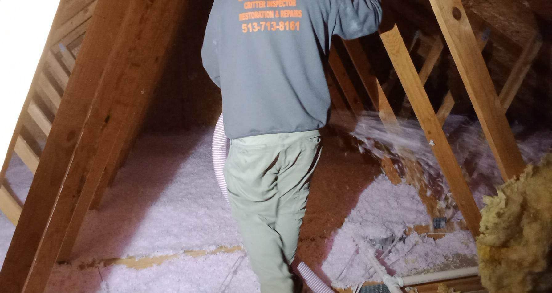 A man in a gray shirt is working in an attic.