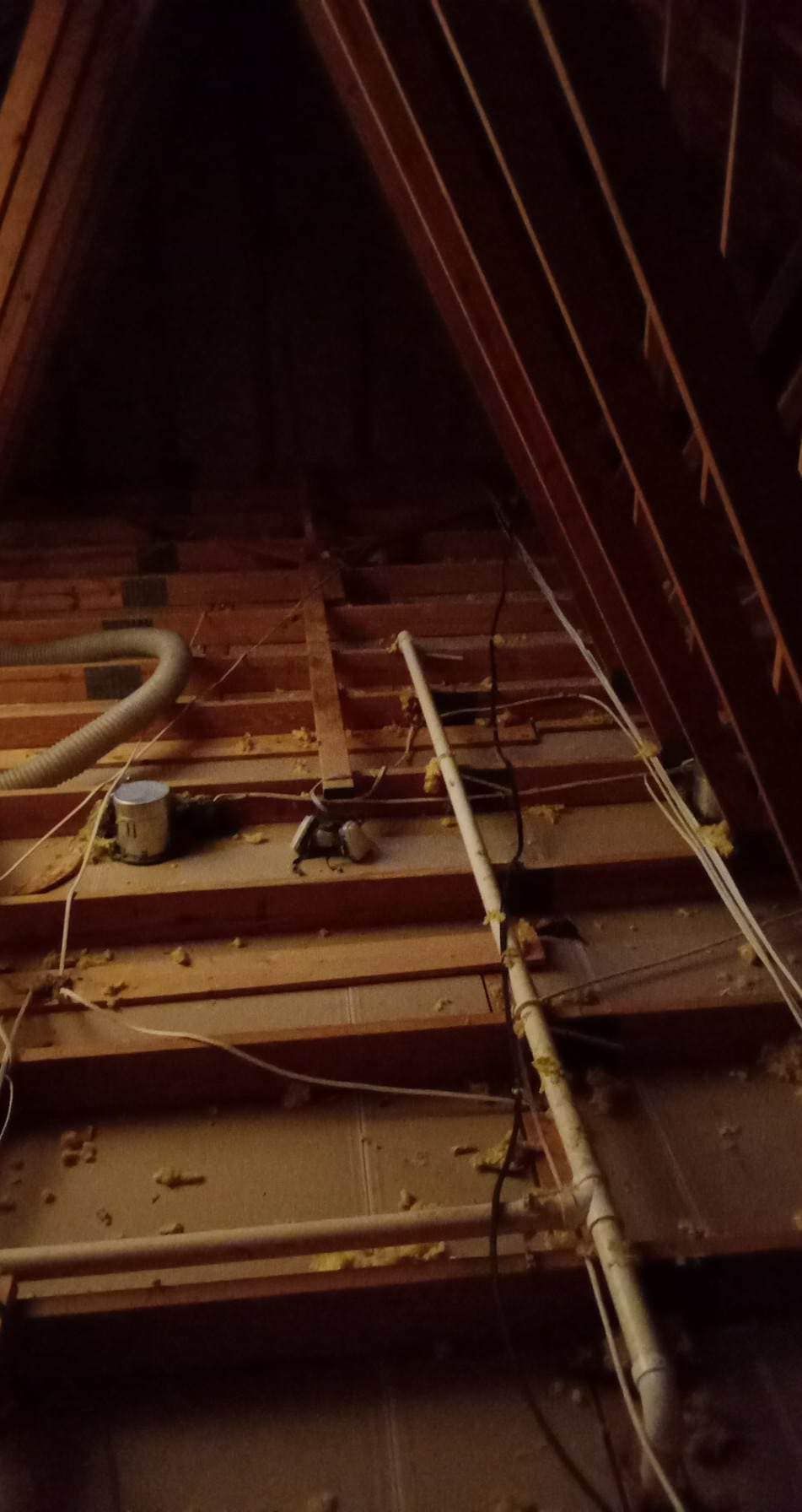 An attic with a lot of pipes and wires hanging from the ceiling.