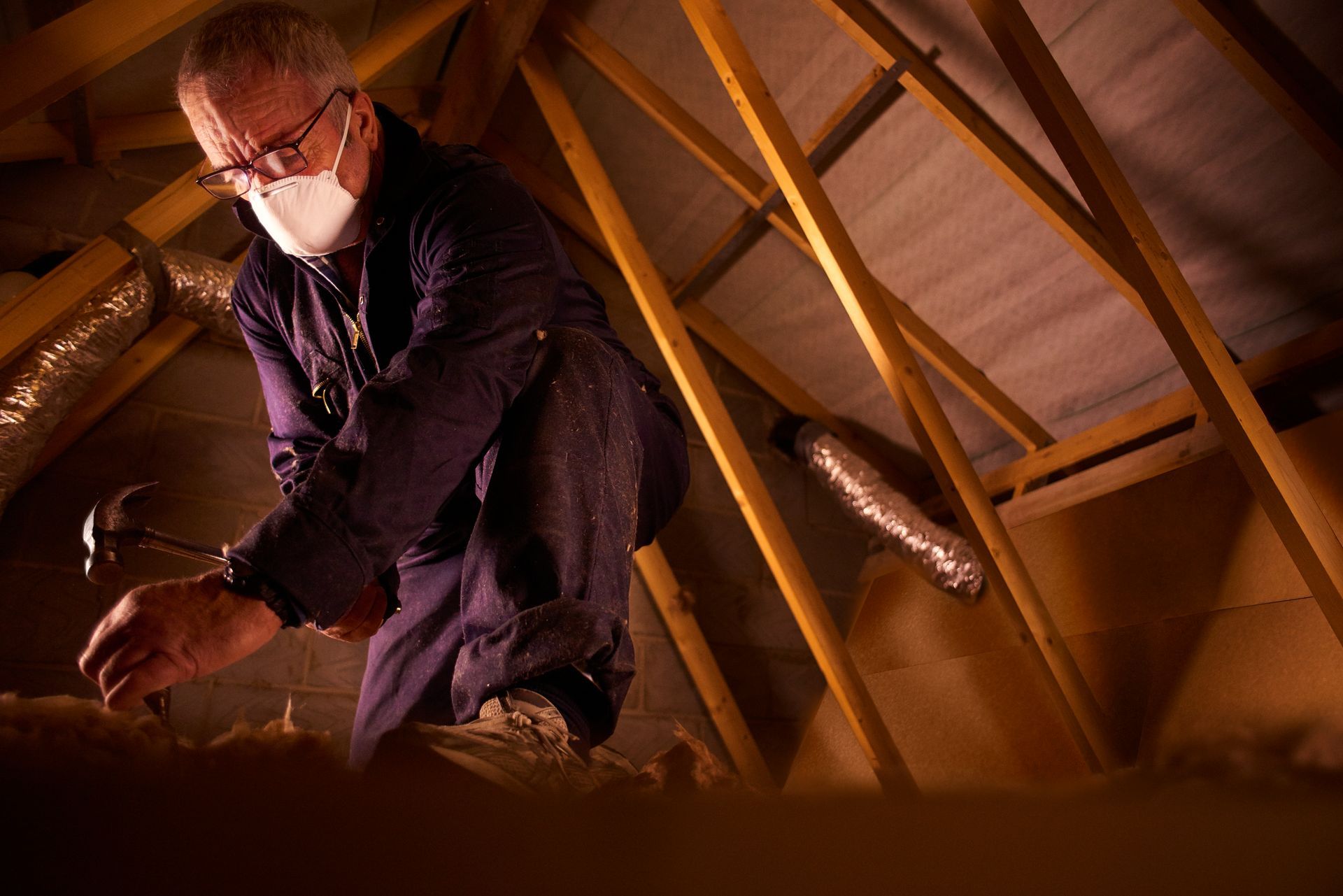 A man wearing a mask is working in an attic.