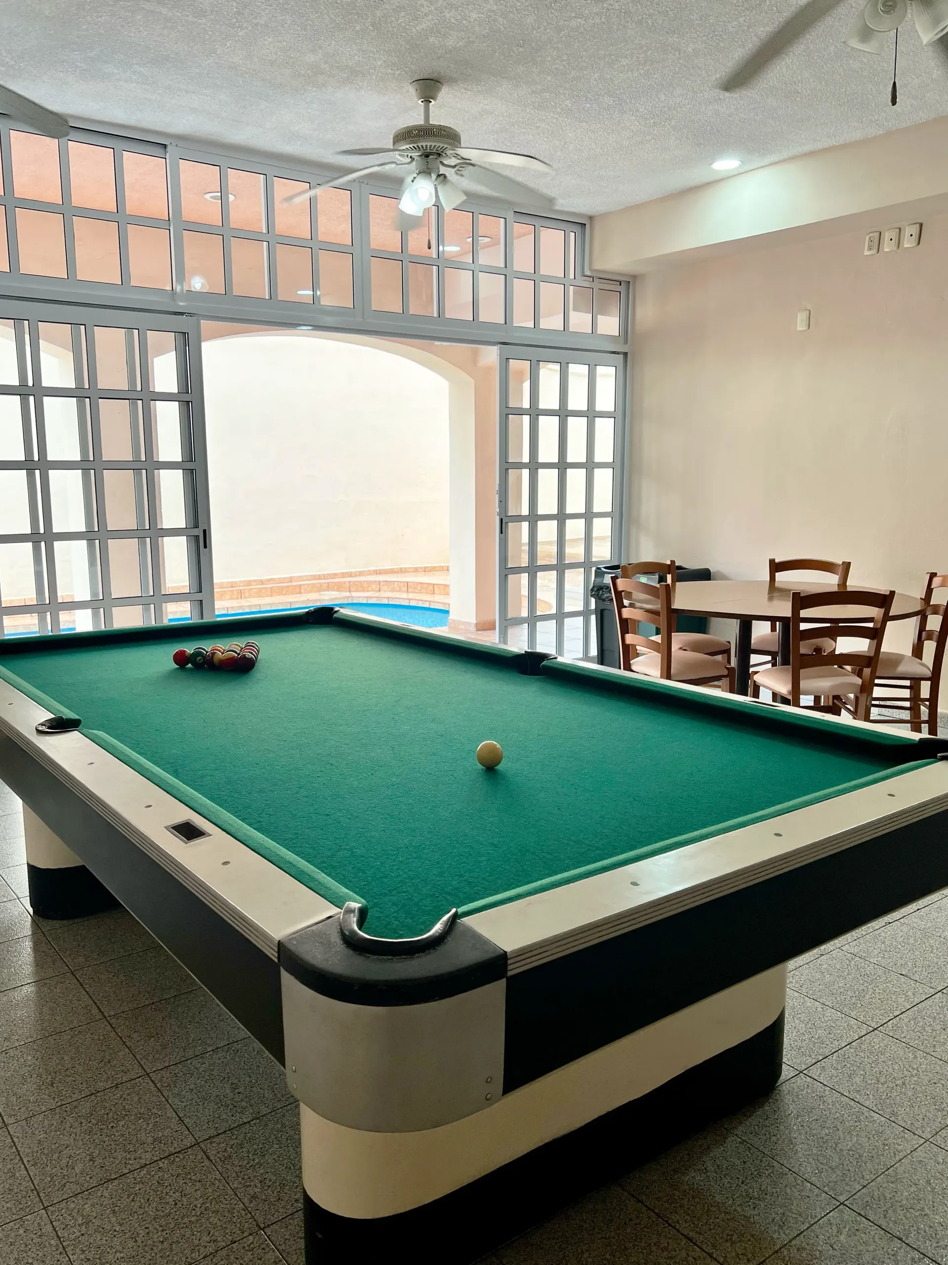 Mesa de billar en una sala con un gran arco que da a la piscina. Juego de comedor a la derecha.