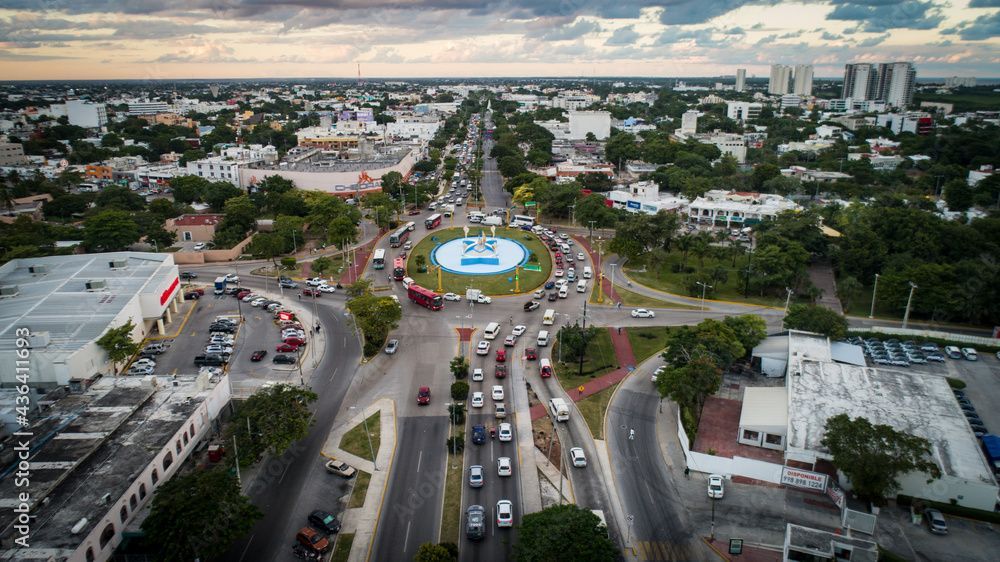 Vista aérea de una rotonda urbana al atardecer, con vehículos circulando por una intersección rodeada de edificios y árboles.