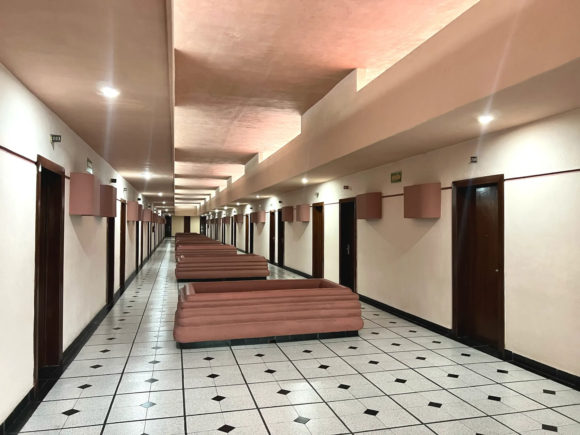 Pasillo largo con puertas, iluminación cenital y bancos. Suelo de baldosas, paredes y techo color melocotón.