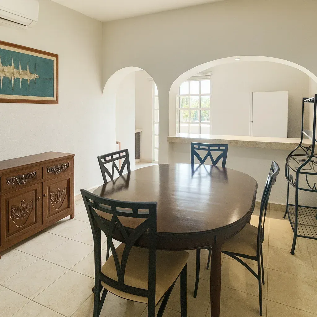 Un comedor con una mesa de madera oscura, cuatro sillas, un armario de madera y puertas arqueadas que dan a una cocina abierta.