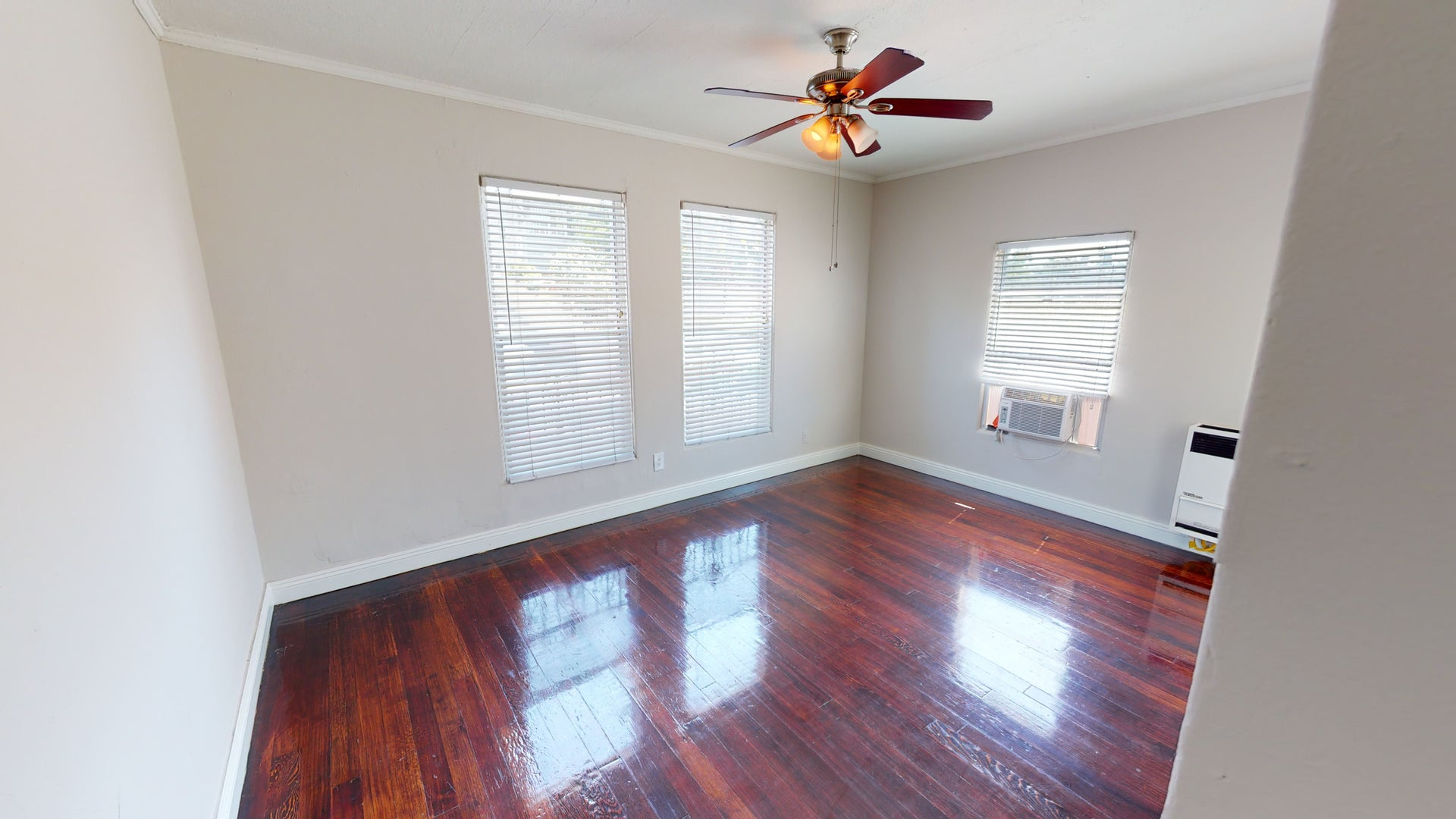 Empty room with dark wood floors, three windows, and a ceiling fan.