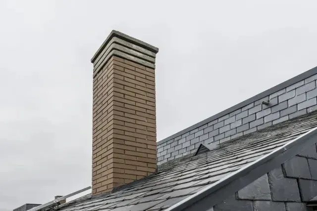 Chimney sweep portland maine - Brick chimney and gray slate roof against a cloudy sky.