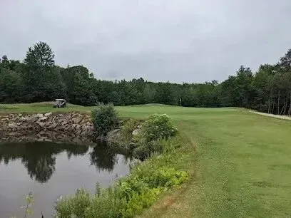 Chimney sweep portland maine- A golf cart sits near a rocky embankment beside a pond on a lush green golf course under a cloudy sky.