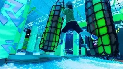 Chimney sweep Portland Maine - A person climbs on a netted obstacle in a brightly lit indoor adventure park.