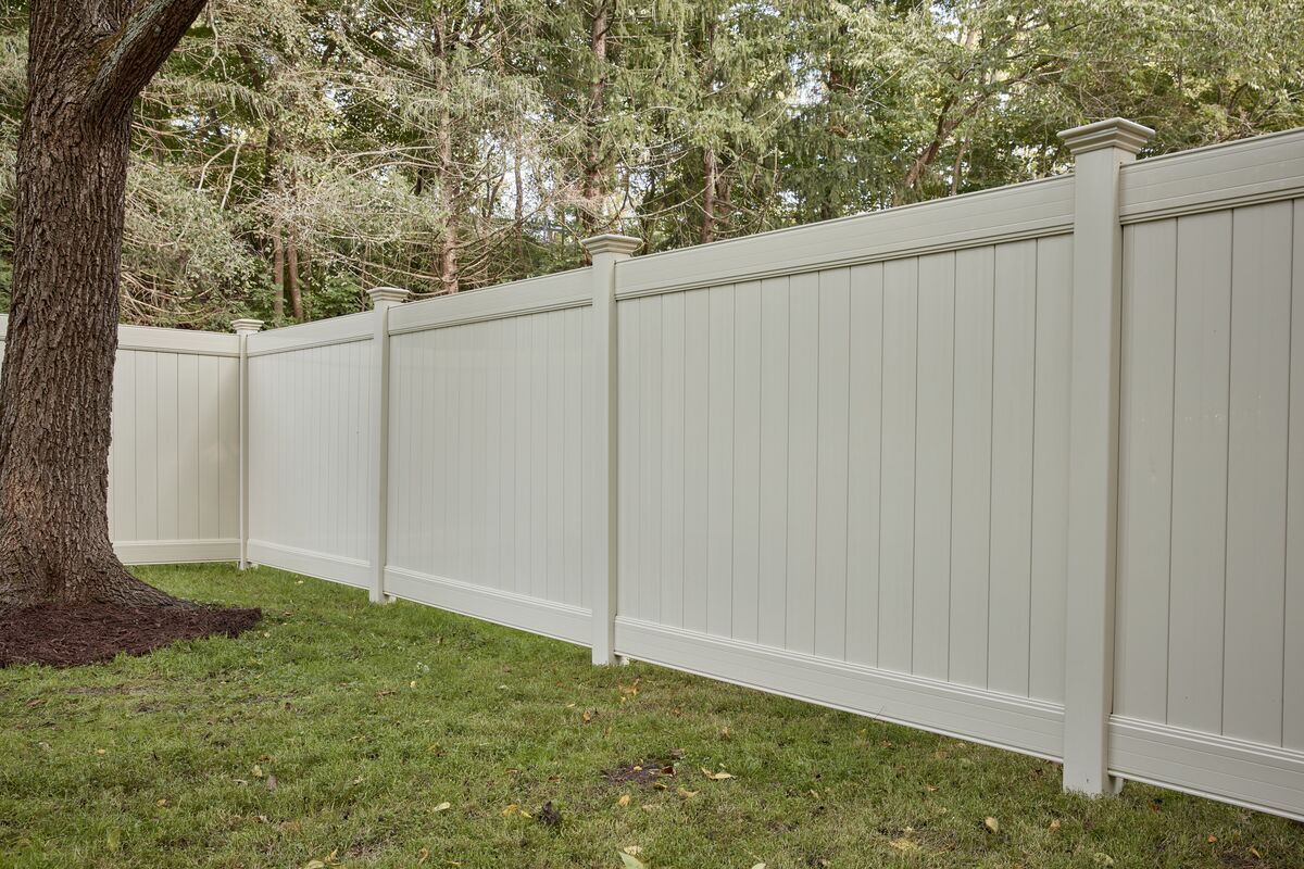 A white vinyl fence is surrounded by grass and trees in a backyard.