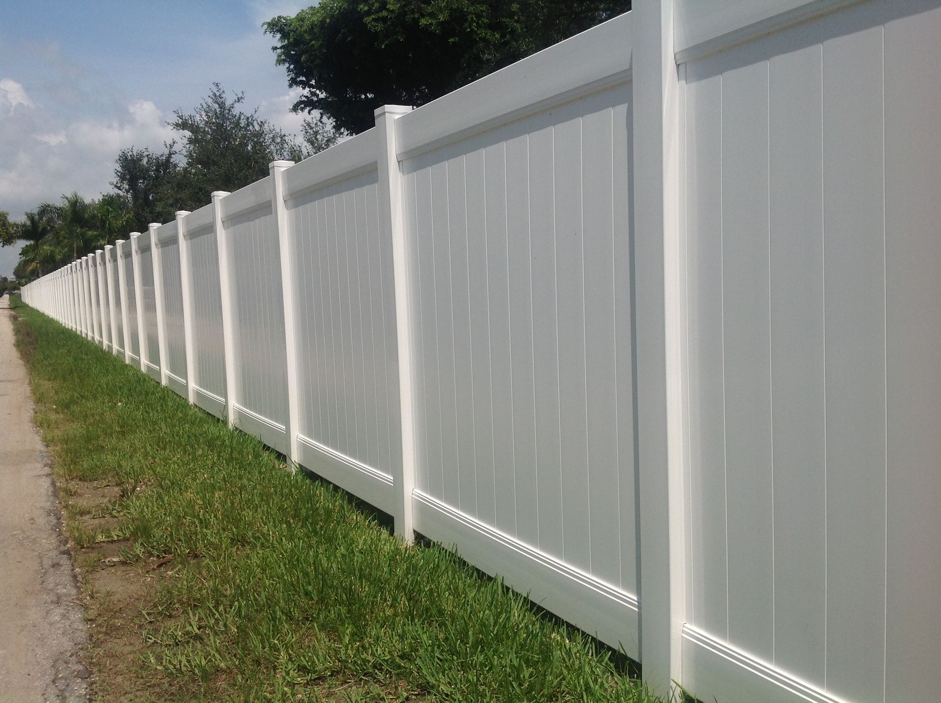 White vinyl privacy fence alongside a sidewalk and grass on a sunny day.