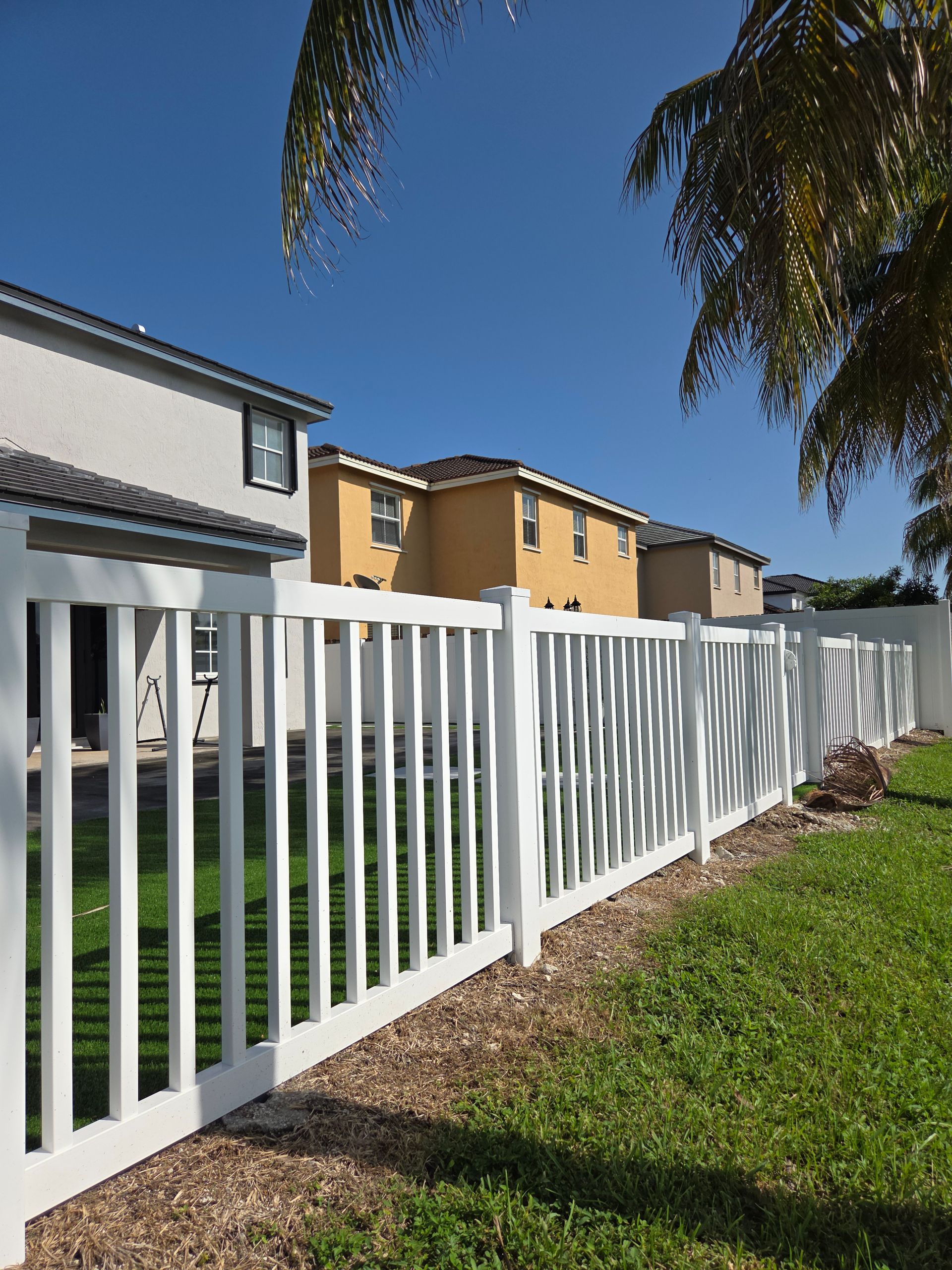 White picket fence with green grass, houses, and a blue sky.