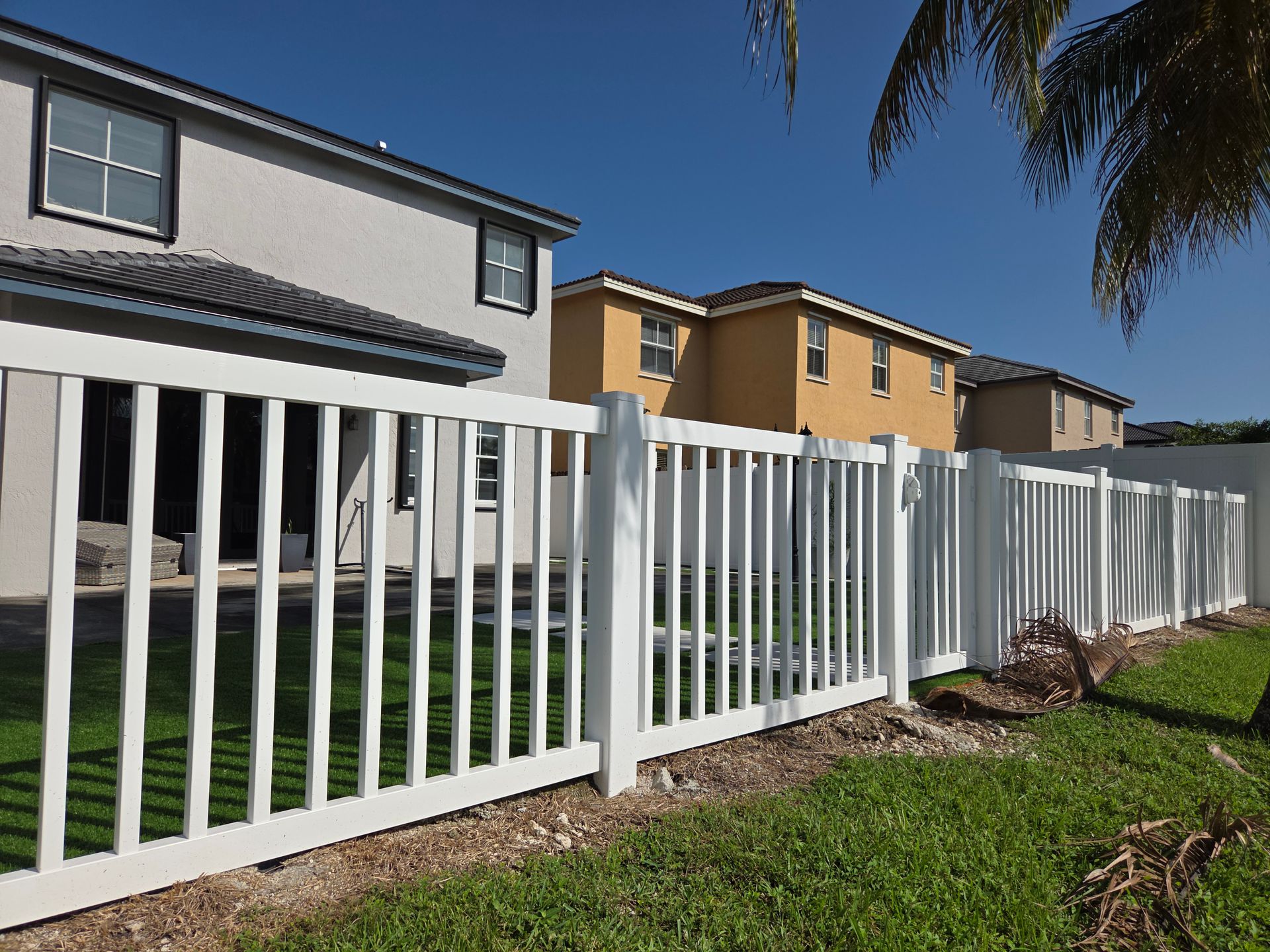 White picket fence in front of beige and yellow houses with blue sky, sunny day.