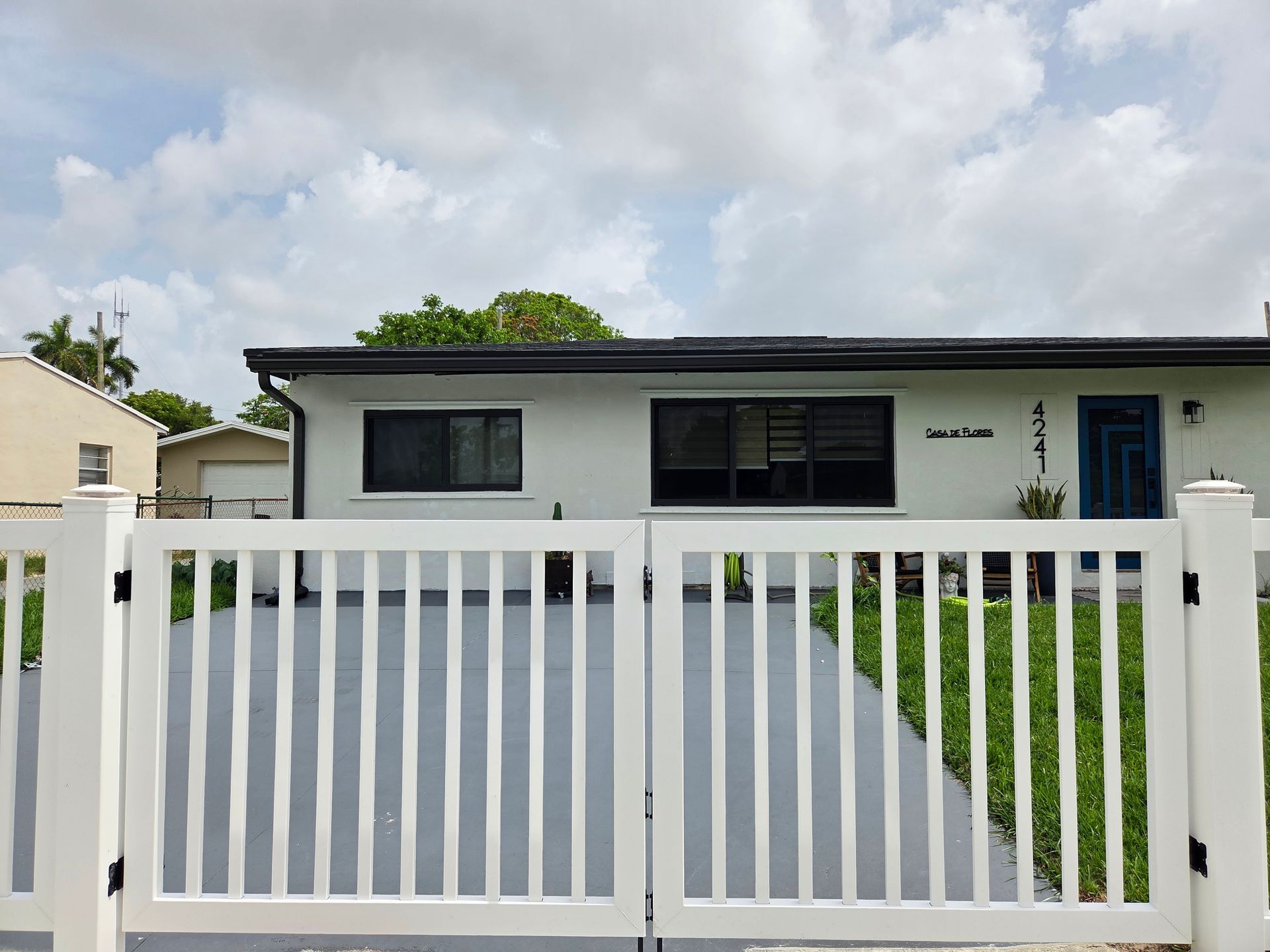 White house with a white picket fence and gray driveway; cloudy sky.