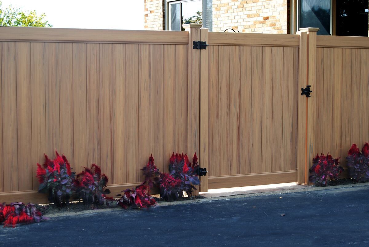 Classic wood grain cypress vinyl privacy fence. A wooden fence with flowers in front of it.