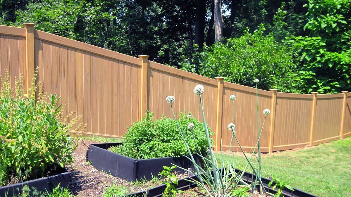 A wooden fence surrounds a garden filled with plants and flowers.