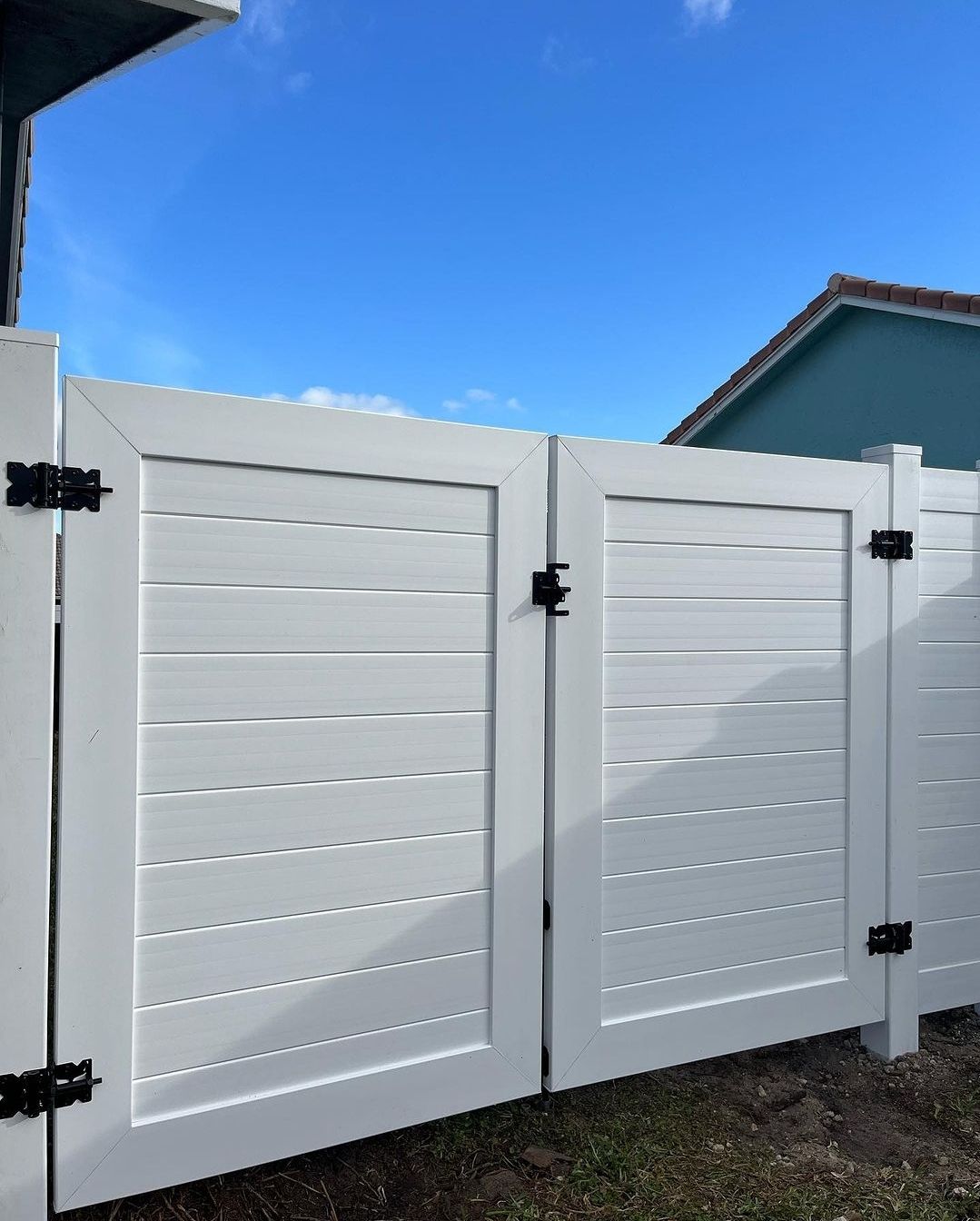 White double gate with black hardware against a blue sky.