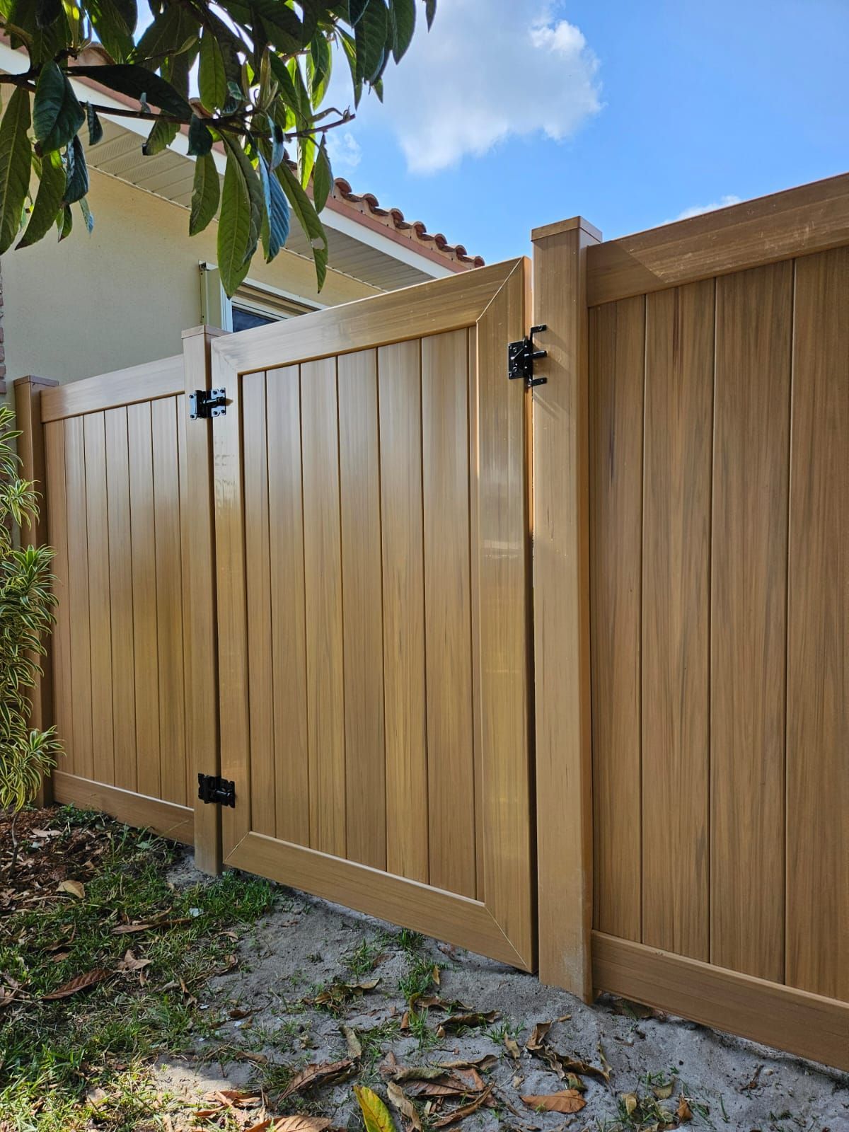 Wooden fence with gate, light brown color, black hinges and latch, in a yard, sunny day.