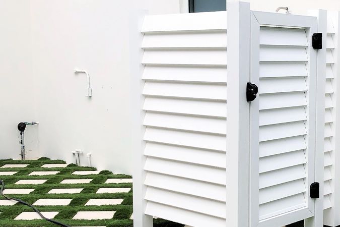 A white outdoor shower with shutters on the side of it.