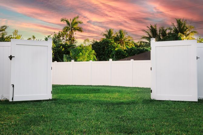 There is a white fence and a gate in the backyard.