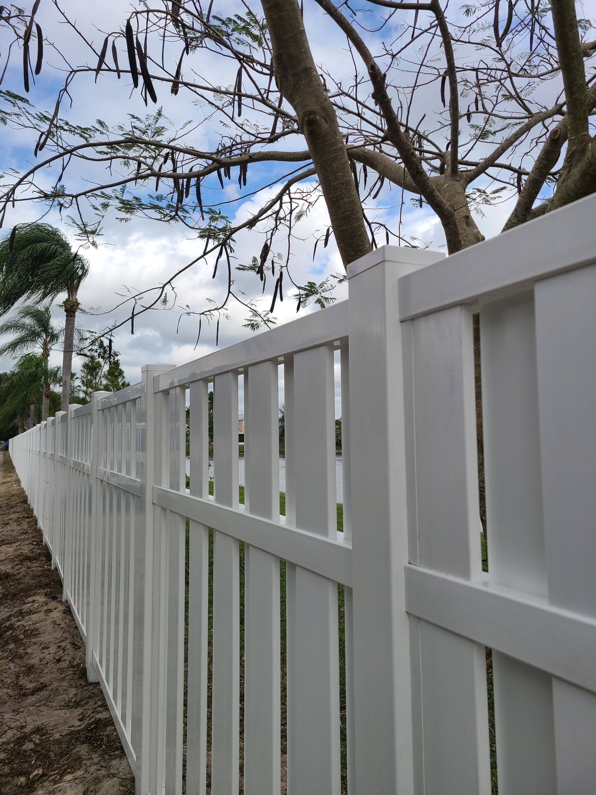 A white fence is surrounded by trees and dirt.