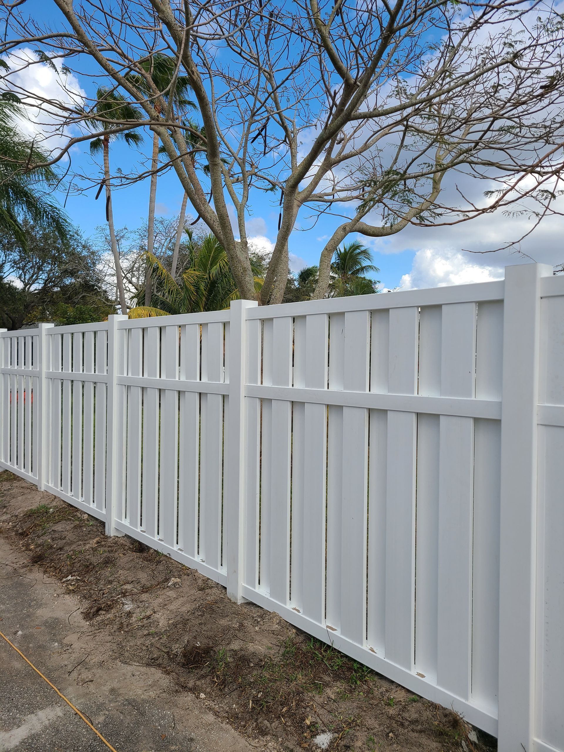 A white wooden fence is surrounded by trees on a sunny day.