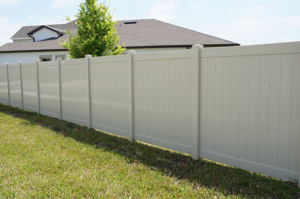 A white vinyl fence surrounds a lush green yard in front of a house.