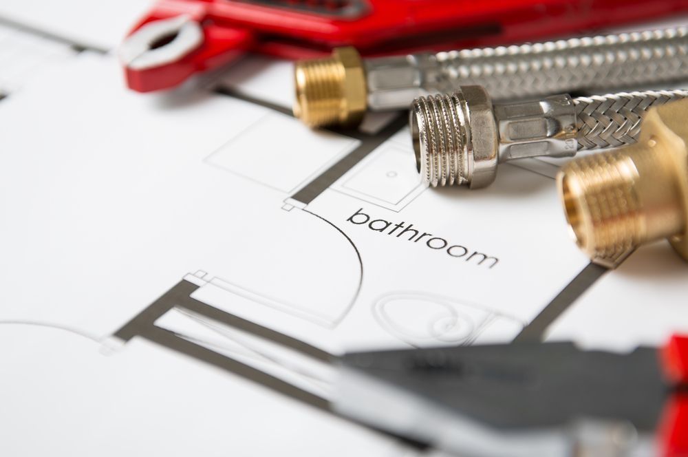 Plumbing tools and braided metal hoses resting on top of a printed bathroom floor plan.