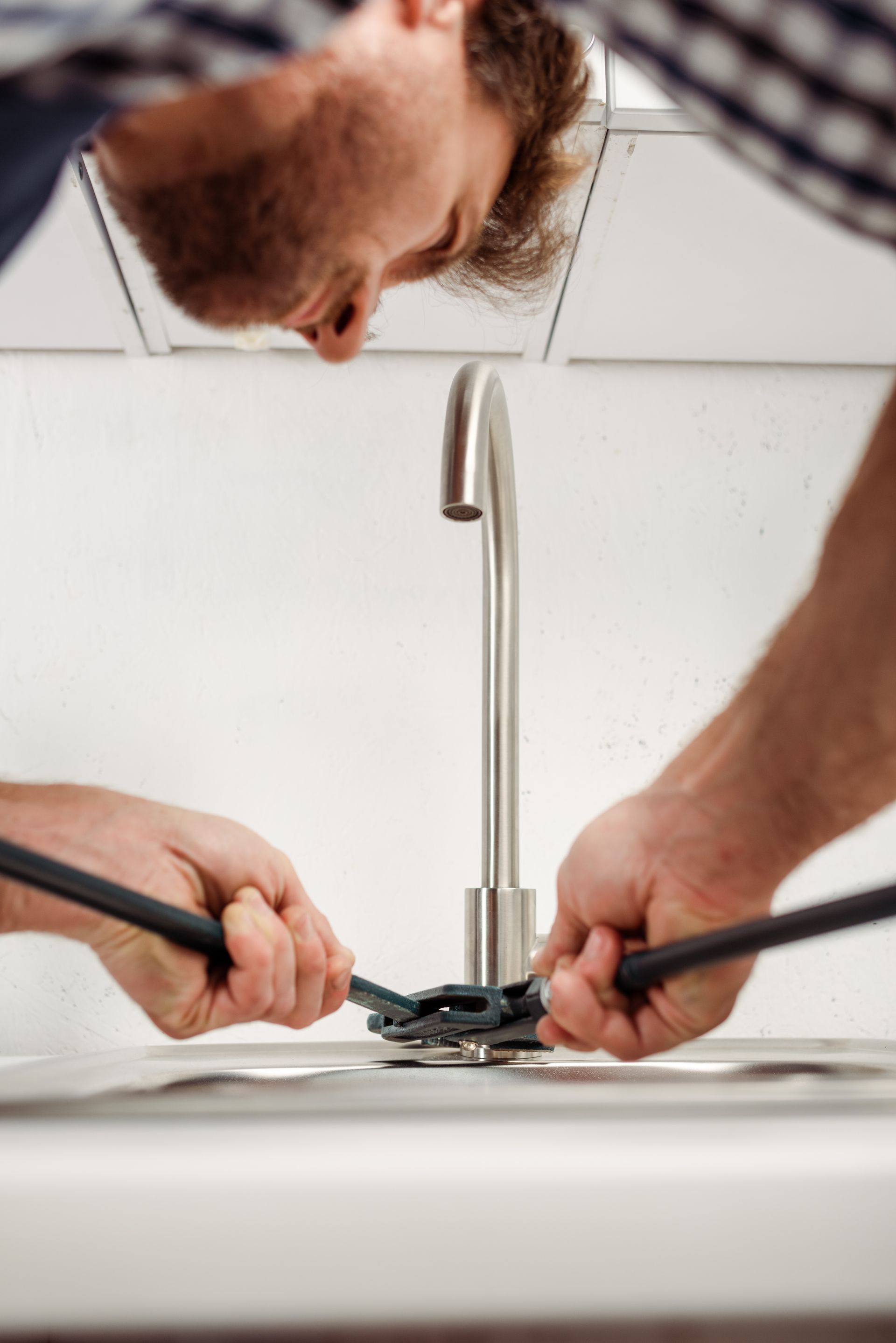 A person works on a kitchen faucet using a tool, viewed from a top-down perspective.