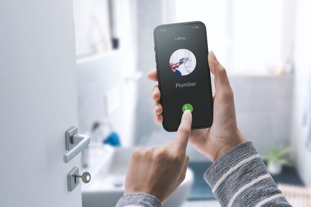 A hand holds a smartphone showing an incoming call, with a finger touching the green accept button in a bright bathroom.