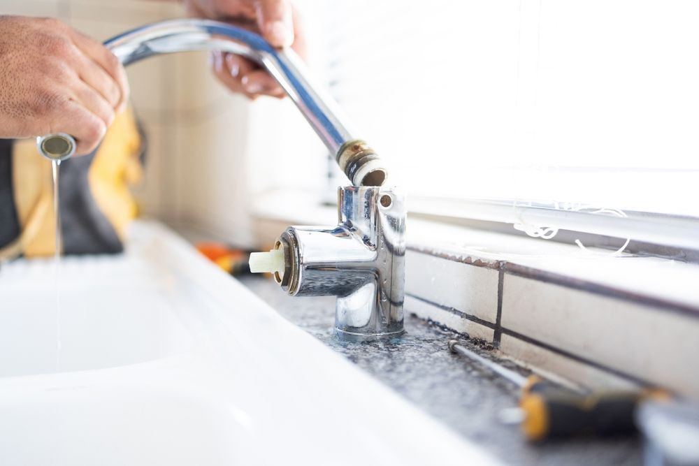 A pair of hands disassembling a chrome kitchen faucet above a sink, with tools nearby.