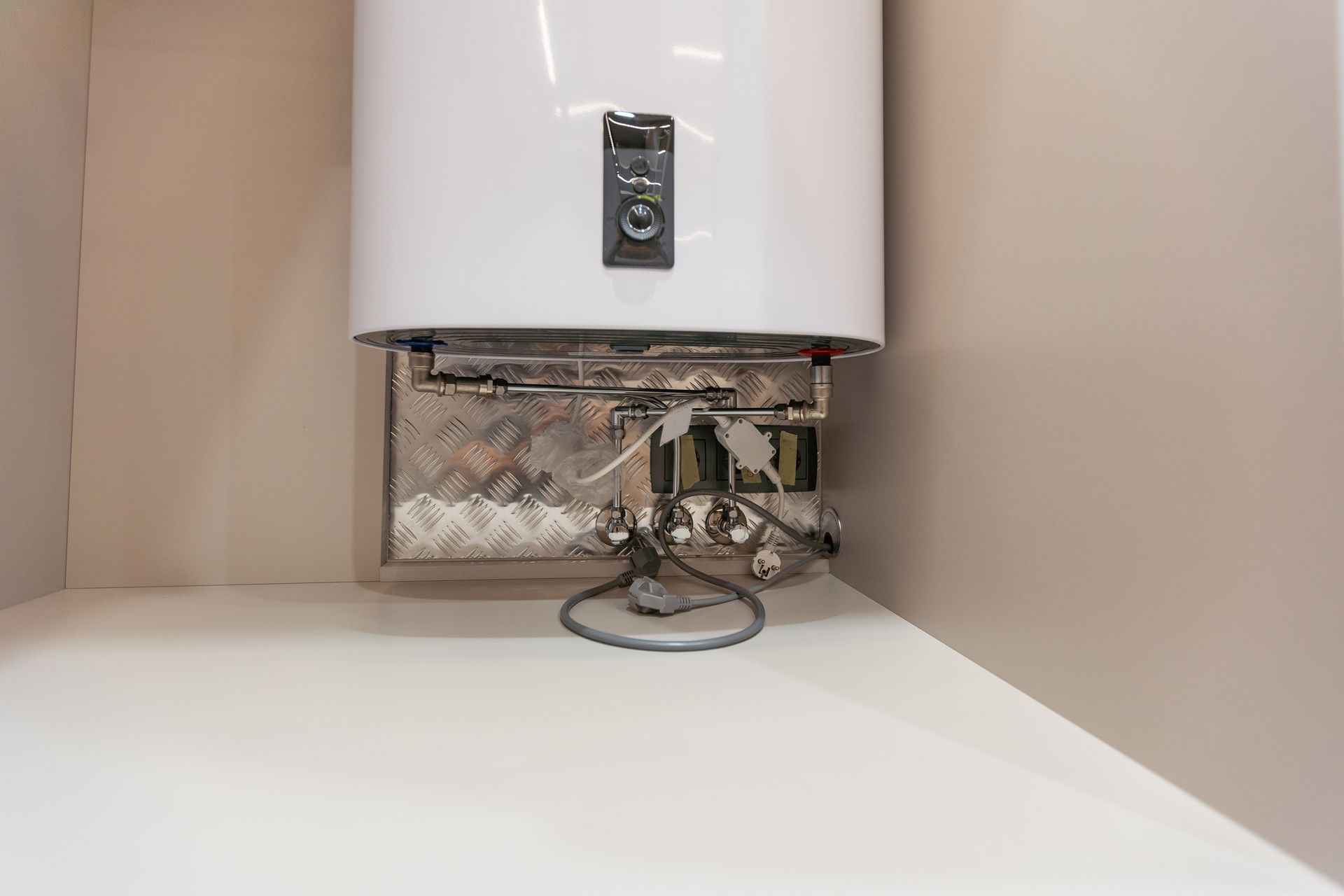 White electric water heater mounted on a wall with exposed metal pipes and connections below.