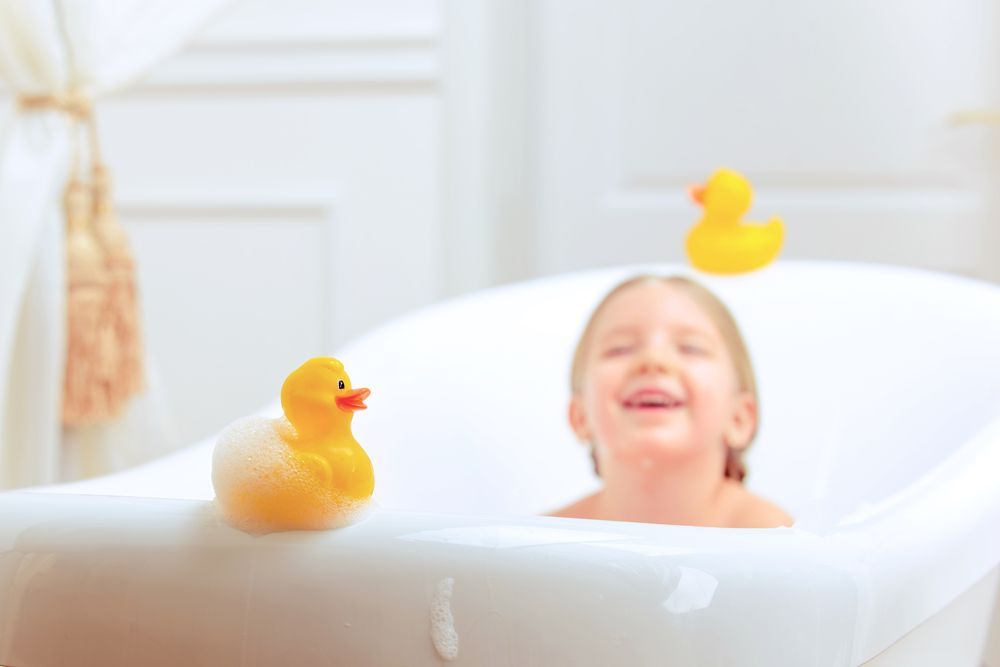 A joyful child sits in a white bathtub with yellow rubber ducks nearby.