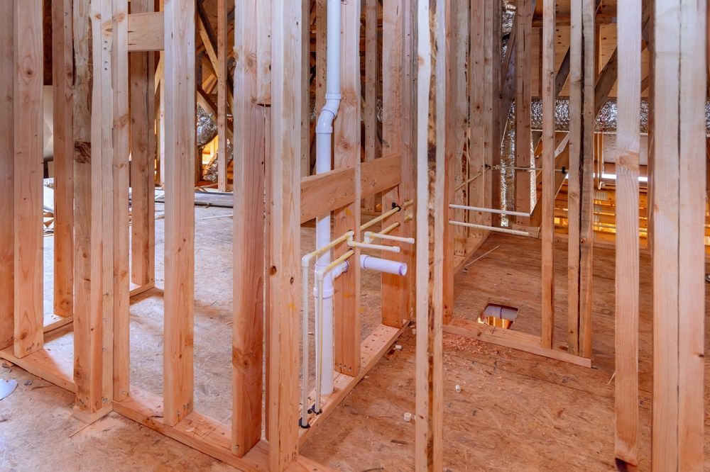A wooden frame construction of a room interior with exposed white plumbing pipes and yellow water supply lines.