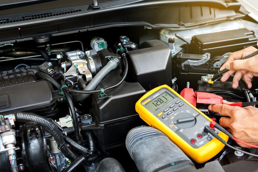 Mechanic Testing a Car Battery With a Yellow Multimeter in the Engine Bay — AA Automotive Repairs in Forster, NSW
